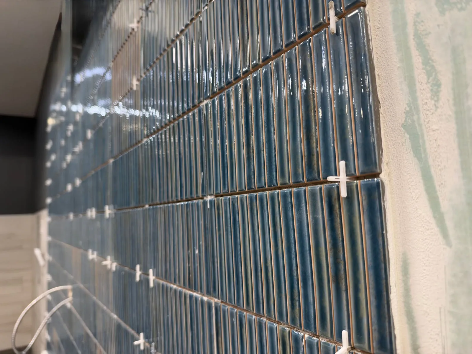 Glossy blue finger-mosaic wall tile mid-installation, spacers still in place